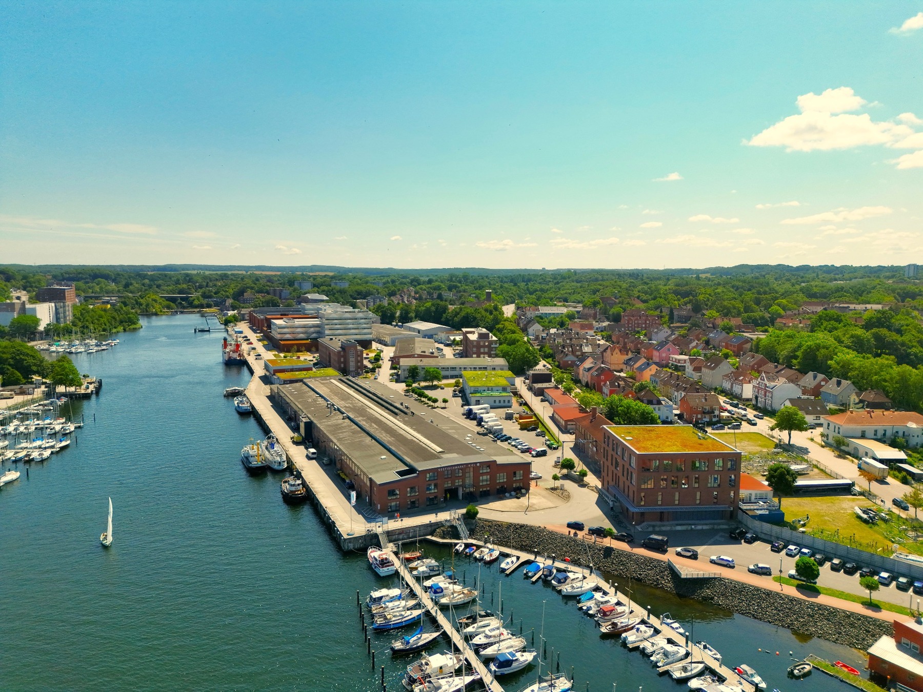 Drohnenaufnahme des Seefischmarkts in Kiel mit Hafenbecken, Booten und Gebäuden